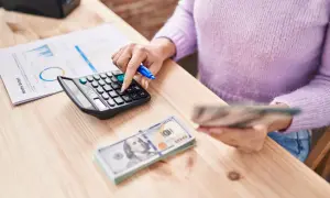 Kobieta liczy pieniądze na kalkulatorze, analizując miesięczny budżet. Zastanawia się, ile się zarabia na pół etatu, by zaplanować wydatki.