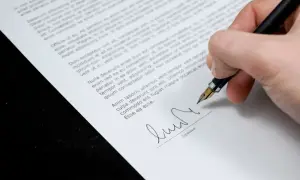 Dłoń podpisuje piórem dokument, prawdopodobnie aneks do umowy o pracę.
