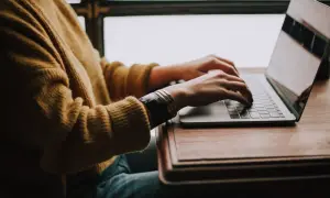 Osoba w żółtym swetrze pisze na laptopie, szukając gotowego wzoru jak napisać CV do pracy.