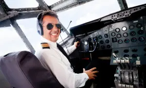 Uśmiechnięty pilot w okularach przeciwsłonecznych i słuchawkach w kokpicie. Zastanawiasz się, ile zarabia pilot samolotu?