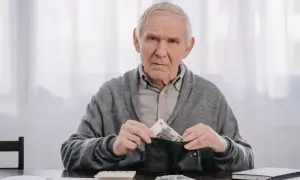 Zmartwiony starszy mężczyzna wkłada pieniądze do portfela, zastanawiając się, kiedy można przejść na wcześniejszą emeryturę.