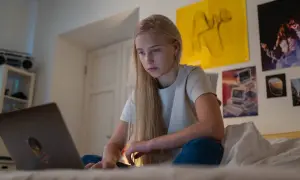 Dziewczyna na łóżku z laptopem. Zastanawia się, od którego roku życia można pracować, szukając informacji w internecie.