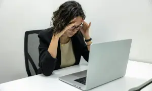 Kobieta z bólem głowy przy laptopie. Zastanawia się, kiedy można zwolnić pracownika zatrudnionego na czas nieokreślony.