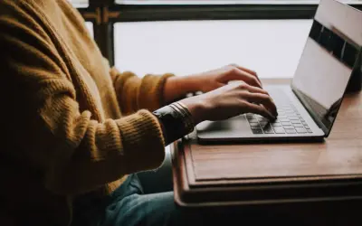 Osoba w żółtym swetrze pisze na laptopie, szukając gotowego wzoru jak napisać CV do pracy.
