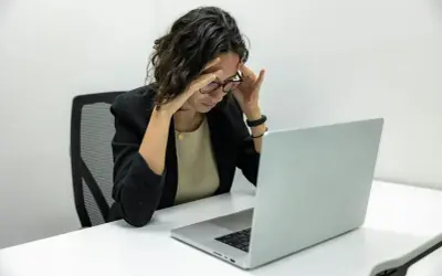 Kobieta z bólem głowy przy laptopie. Zastanawia się, kiedy można zwolnić pracownika zatrudnionego na czas nieokreślony.