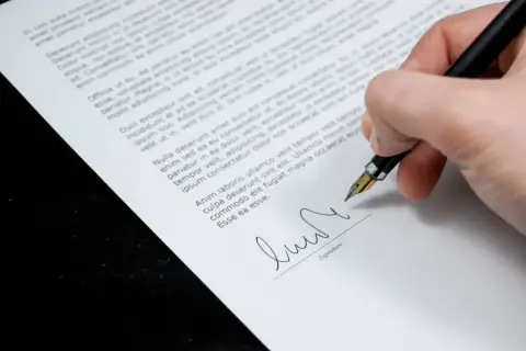 Dłoń podpisuje piórem dokument, prawdopodobnie aneks do umowy o pracę.