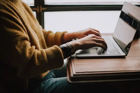 Osoba w żółtym swetrze pisze na laptopie, szukając gotowego wzoru jak napisać CV do pracy.