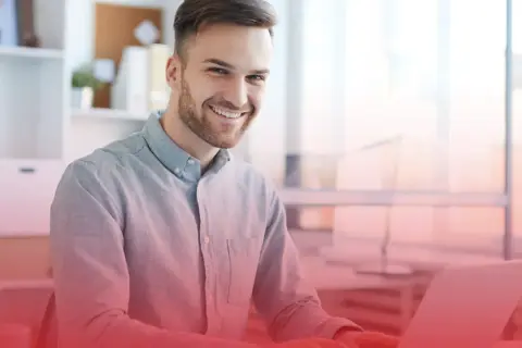 Uśmiechnięty mężczyzna przy laptopie. Szukasz odpowiedzi, co napisać w CV jeśli nie masz żadnego doświadczenia?