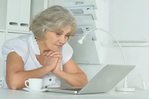 Starsza pani z zaciekawieniem patrzy na laptopa, szukając informacji, ile trwa staż z urzędu pracy.