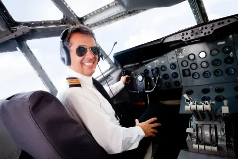 Uśmiechnięty pilot w okularach przeciwsłonecznych i słuchawkach w kokpicie. Zastanawiasz się, ile zarabia pilot samolotu?