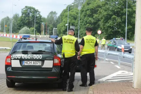 Funkcjonariusze Służby Celno-Skarbowej w kamizelkach odblaskowych przy radiowozie. Ich praca to nie tylko służba, ale też zarobki.