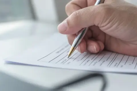 Dłoń pisze długopisem na kwestionariuszu osobowym dla pracownika.