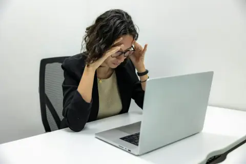 Kobieta z bólem głowy przy laptopie. Zastanawia się, kiedy można zwolnić pracownika zatrudnionego na czas nieokreślony.