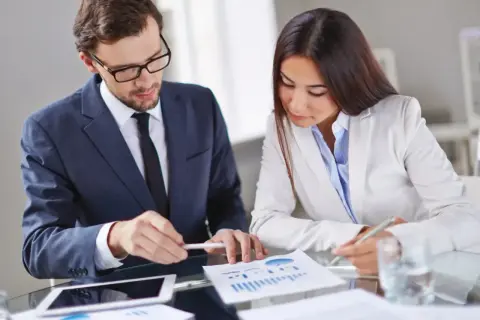 Mężczyzna w okularach i garniturze, który jest brokerem, analizuje wykresy z kobietą.