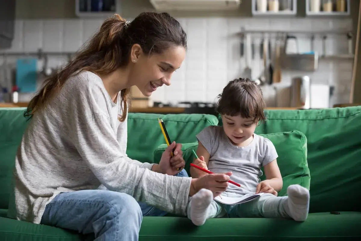Uśmiechnięta mama pomaga dziecku w rysowaniu. Wspólna praca dla dzieci, rozwijająca kreatywność i więź.