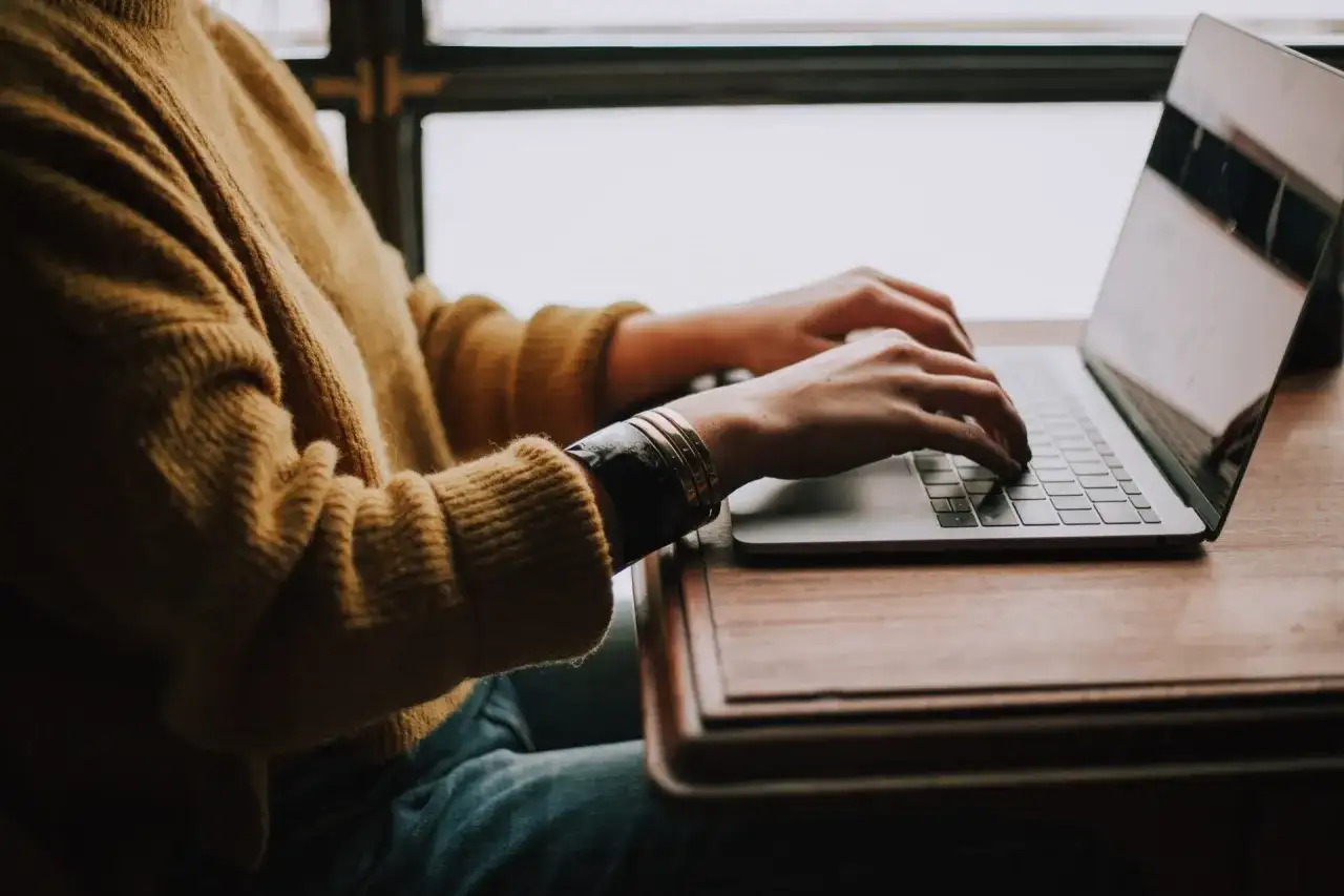 Osoba w żółtym swetrze pisze na laptopie, szukając gotowego wzoru jak napisać CV do pracy.