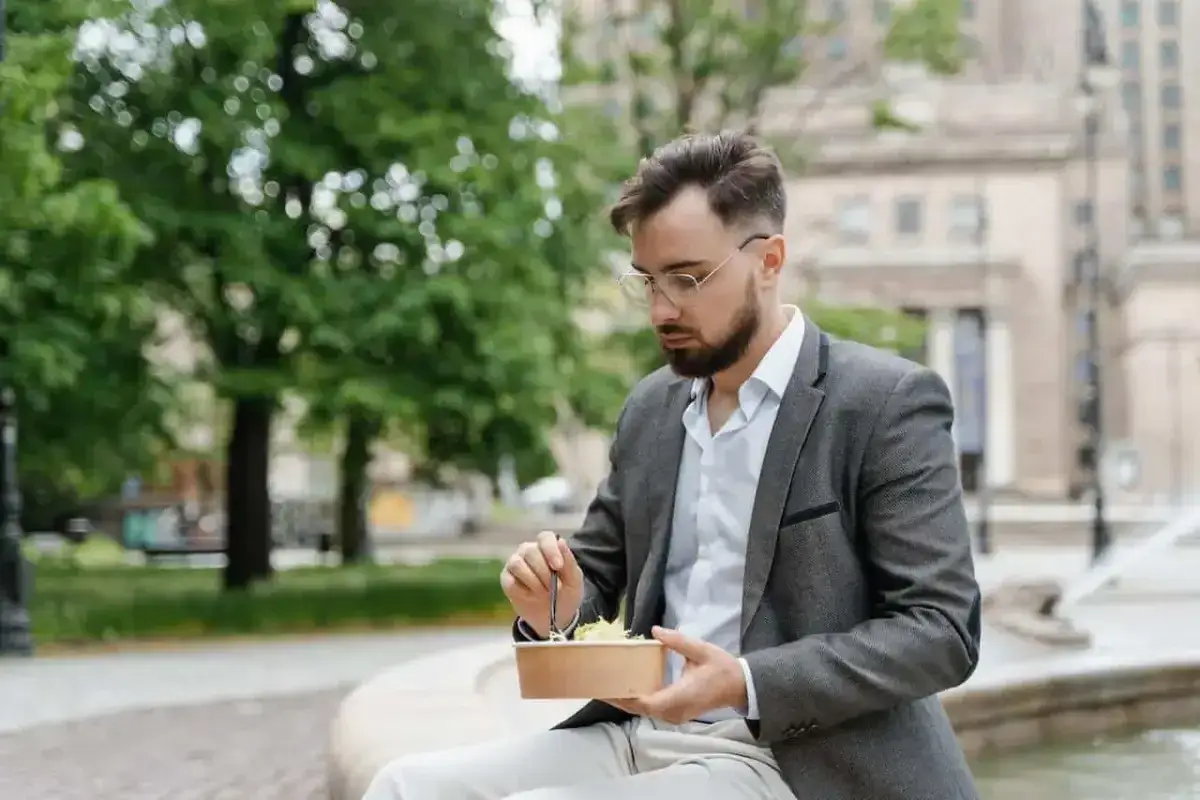 Mężczyzna w garniturze je sałatkę na ławce. Czy to jego przerwa w pracy?