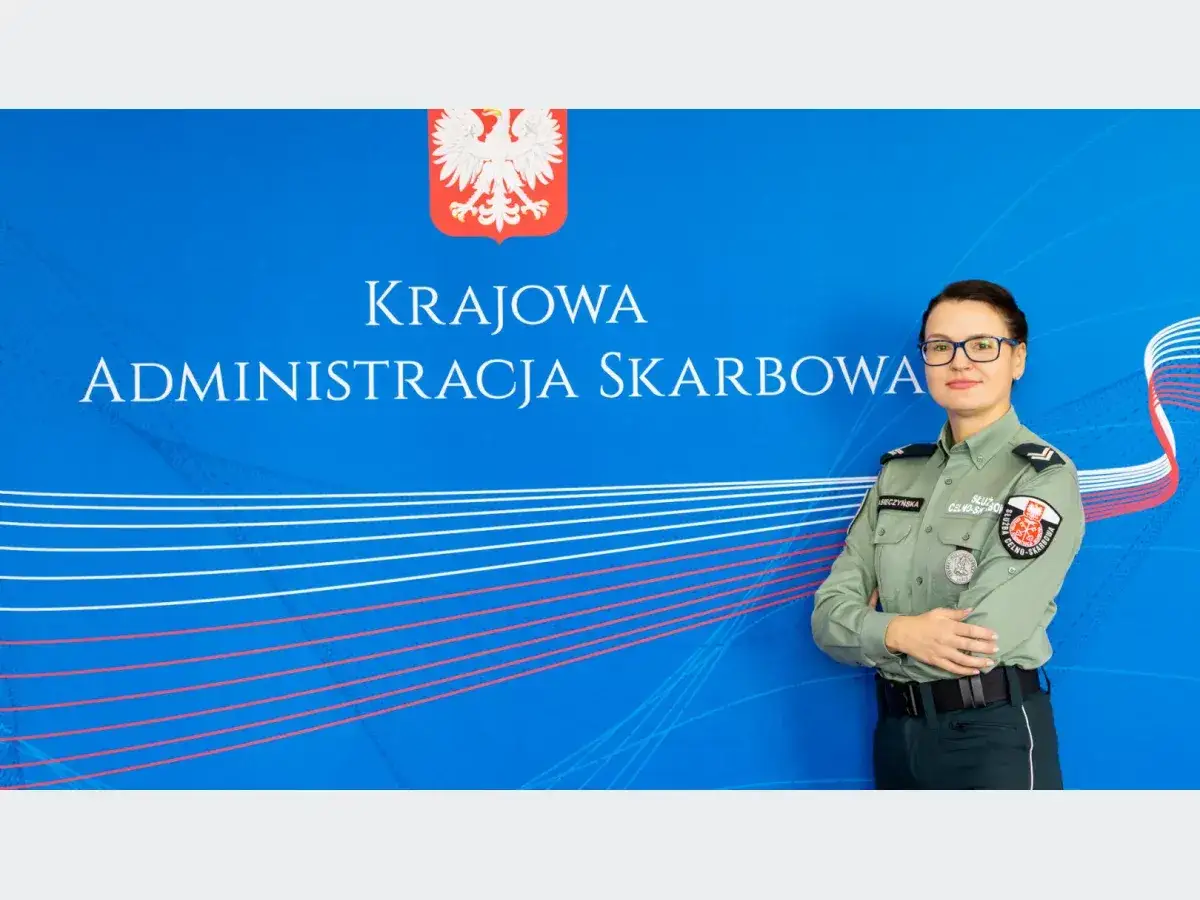 Kobieta w mundurze Służby Celno-Skarbowej pozuje na tle niebieskiej ściany z logo KAS. Nabór do służby celnej trwa!