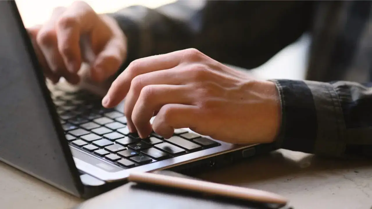 Dłonie piszą na klawiaturze laptopa. To praca zdalna, która może być dobrze płatne i ciekawe zawody.