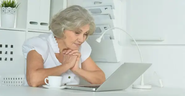 Starsza pani z zaciekawieniem patrzy na laptopa, szukając informacji, ile trwa staż z urzędu pracy.