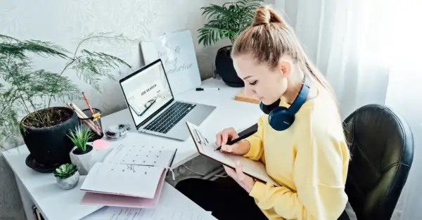 Kobieta pracuje nad CV, szukając pracy. Na biurku laptop z napisem "Job Search", kalendarz i notatnik.