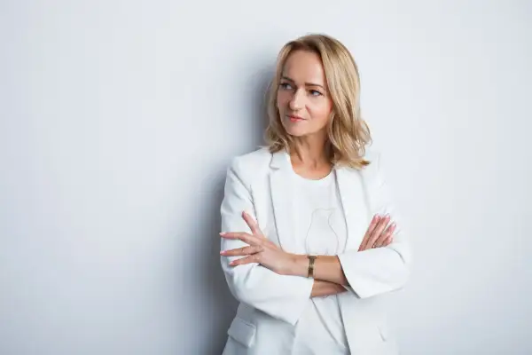 Profesjonalne zdjęcie do CV: kobieta w białej marynarce, z rękami skrzyżowanymi na piersi, patrzy w bok.